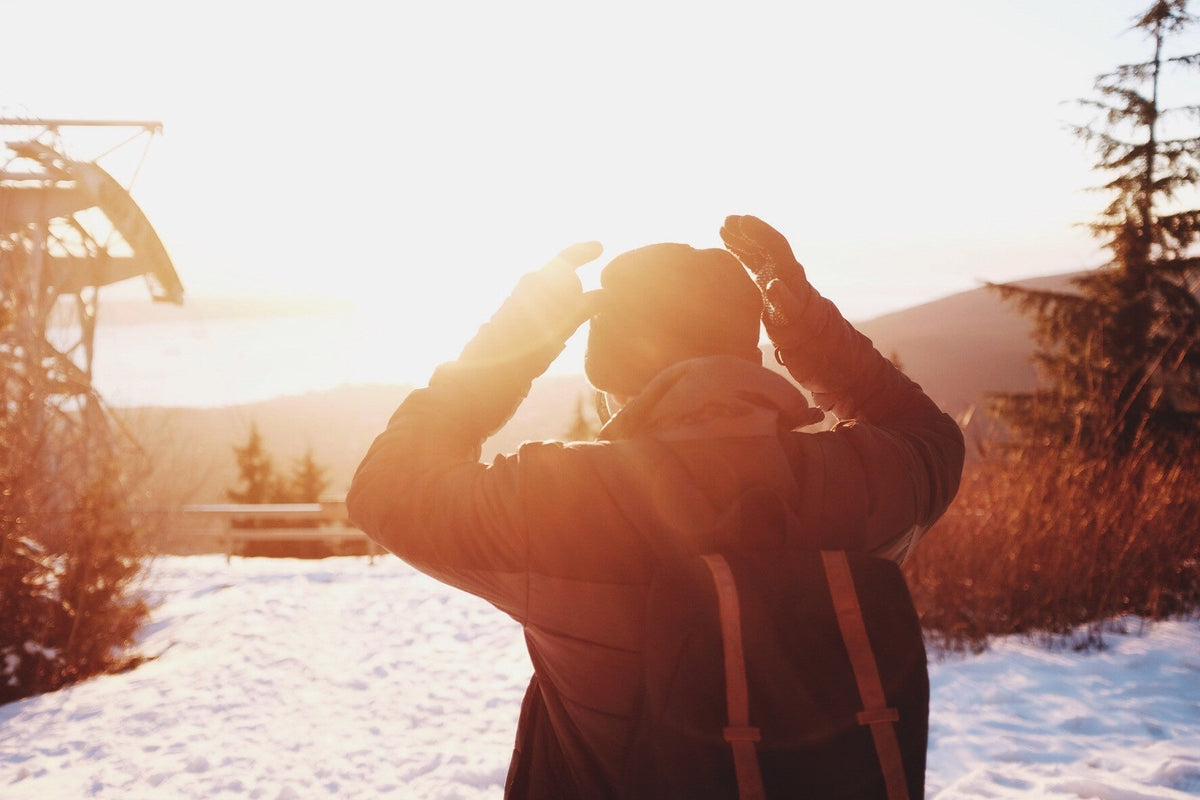 Person in winter gear taking a photo of a snowy mountain landscape at sunset